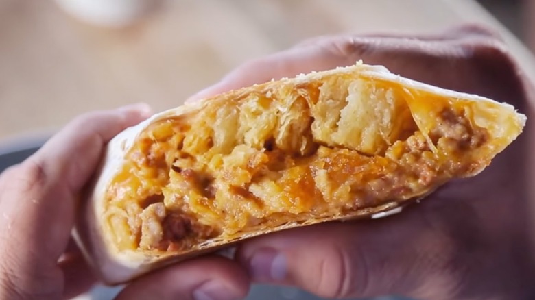 Hands holding biscuits and gravy burrito