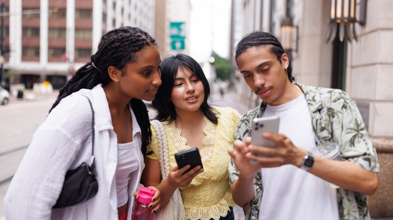 Three people looking at a phone in a city