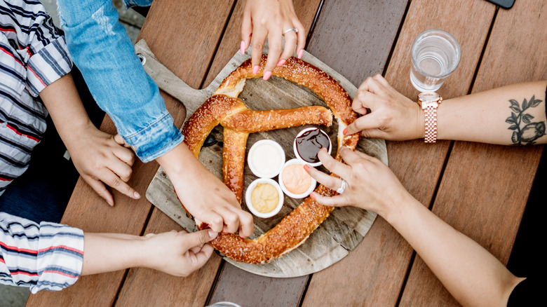 Overhead shot of three pairs of female hands sharing a giant pretzel