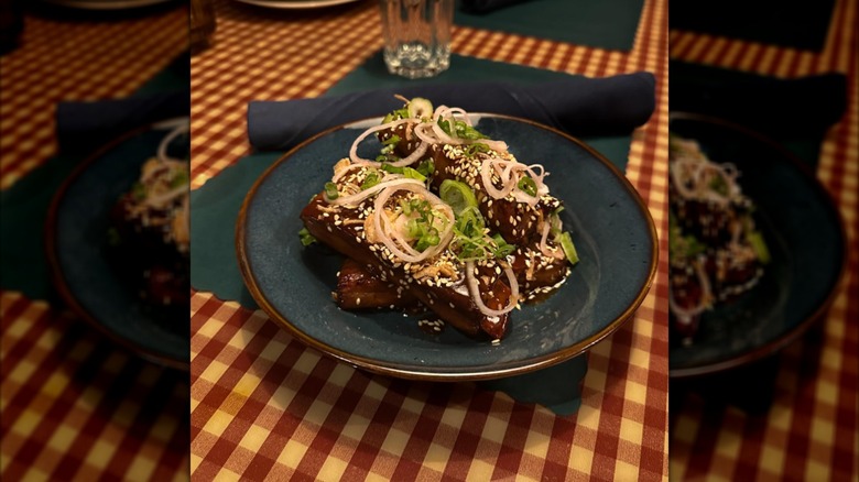 Saucy Asian short ribs on a blue plate inside a restaurant.