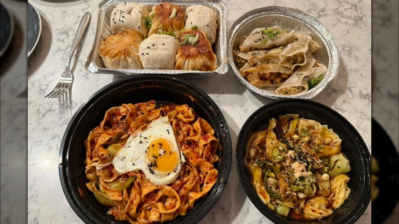 Four takeout containers filled with bao, noodles, and dumplings.