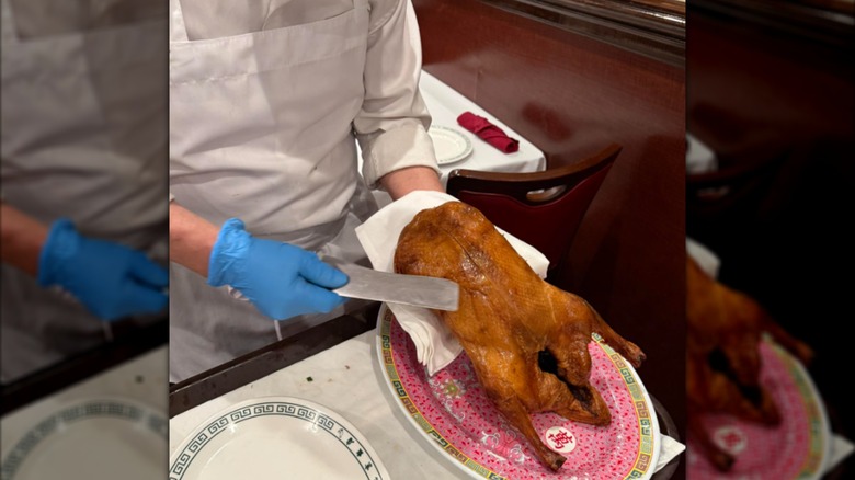 Someone in blue gloves and a white apron carving Peking duck inside a restaurant.