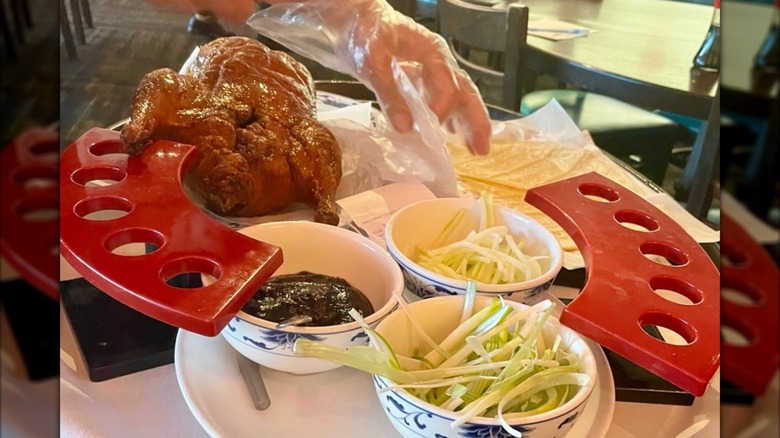 A restaurant server handling a tray with duck, sauce, and vegetables.