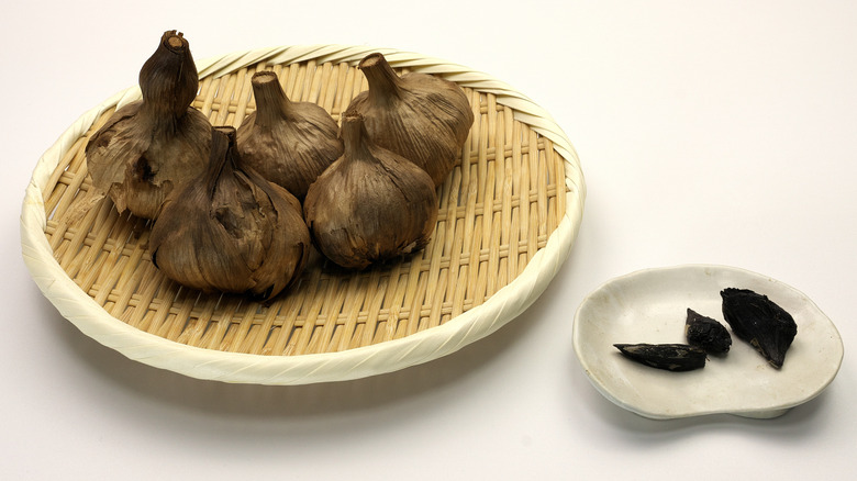 Several bulbs of black garlic in a dish with some cloves in another dish