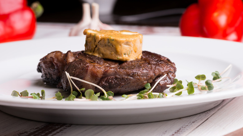 A cooked steak on a white plate topped with a flavored compound butter