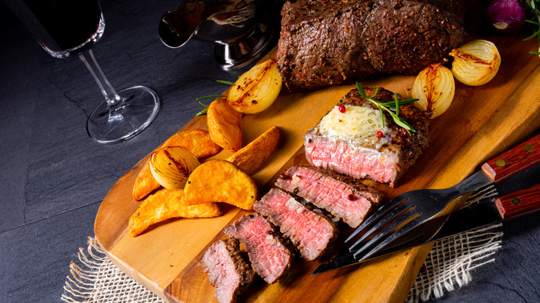Sliced beef steak with butter, herbs, and potato wedges with a glass of red wine