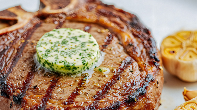 Grilled ribeye steak topped with herb butter, served with roasted garlic cloves