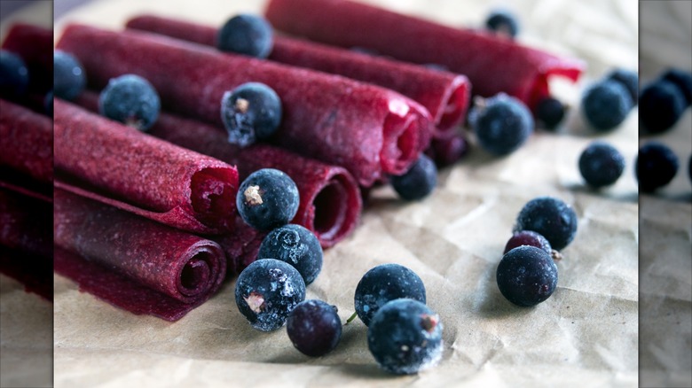 Homemade blueberry fruit leather roll snacks on wax paper next to fresh blueberries