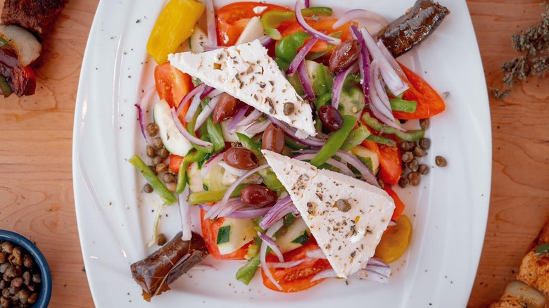 A large plate of mixed vegetables, olives, capers, and feta cheese.
