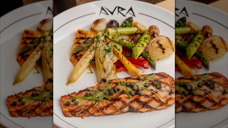 A plate labeled "Avra" loaded with grilled vegetables and fish.