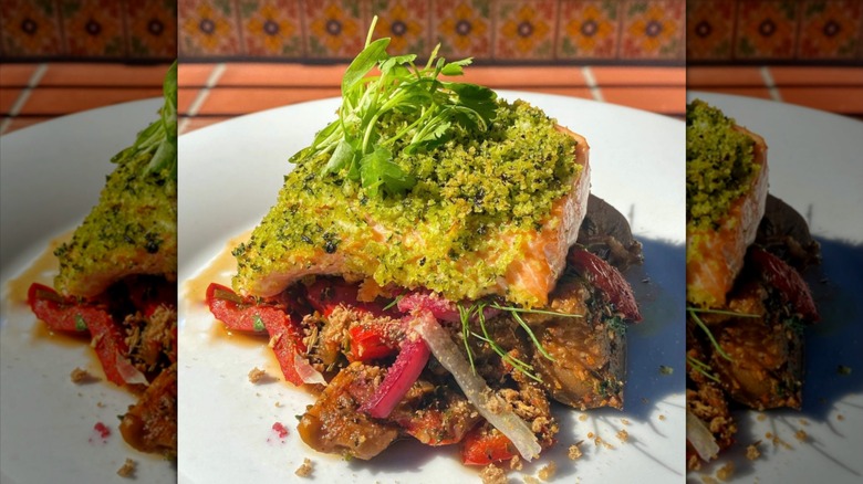 Herb-crusted salmon, vegetables, and fresh herbs on a white plate.