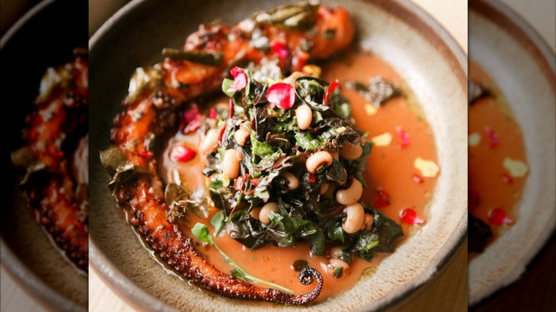 A hearty bowl of red octopus soup topped with greens.