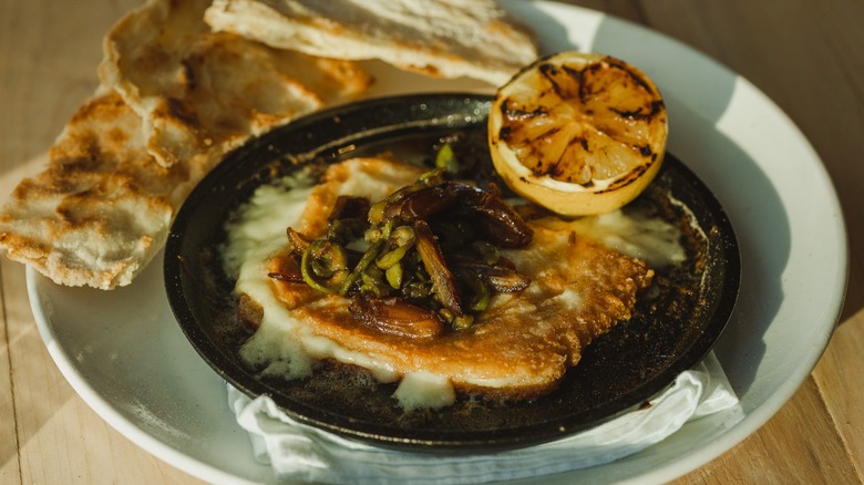 A black bowl of soup topped with seared cheese placed on a white plate with bread.