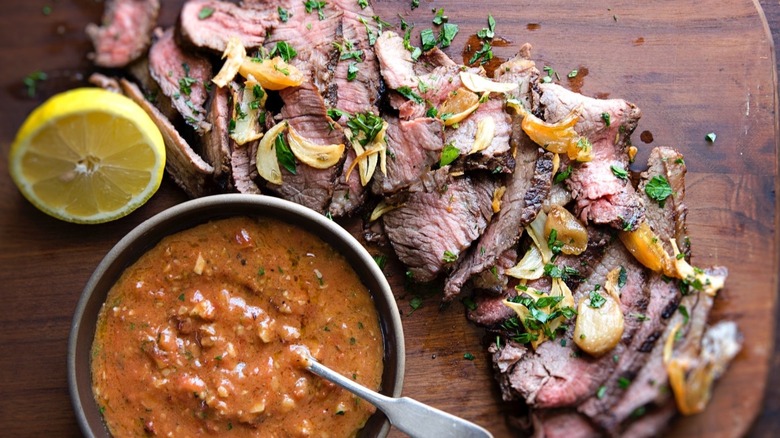 Chopped beef splayed on a wooden cutting board next to a bowl of orange sauce and half lemon.