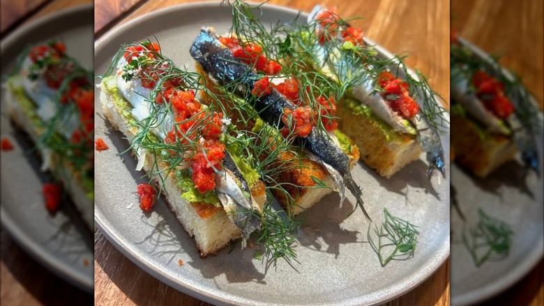An avocado sardine toast plate artfully plated with fresh herbs at Nikos Greek restaurant in Durham