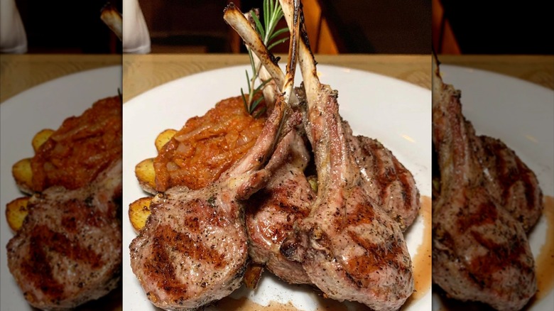 A rack of grilled lamb chops perched over potates.