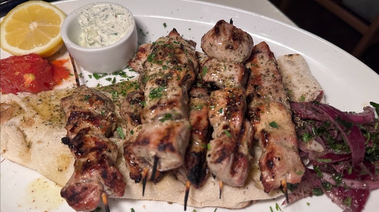 A large plate full of chicken kabobs, sauce, and pita bread resting on a table.