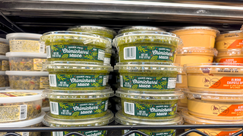 Small tubs of Trader Joe's Chimichurri stacked in towers on refrigerated shelves next to other dips