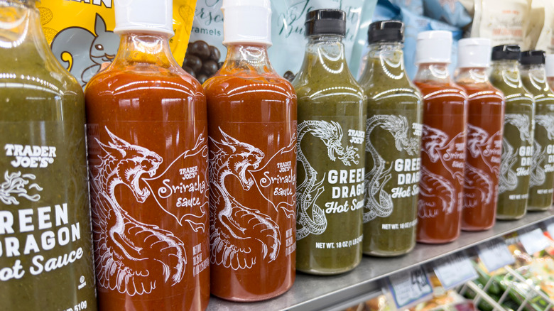 Bottles of Trader Joe's Green Dragon and Sriracha Sauces lined up on grocery store shelves