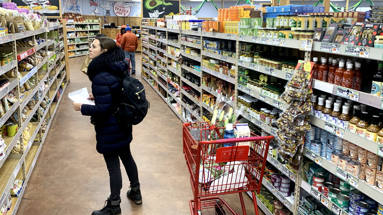 Woman browses selection at Trader Joe's with shopping cart in aisle of sauces and dried goods