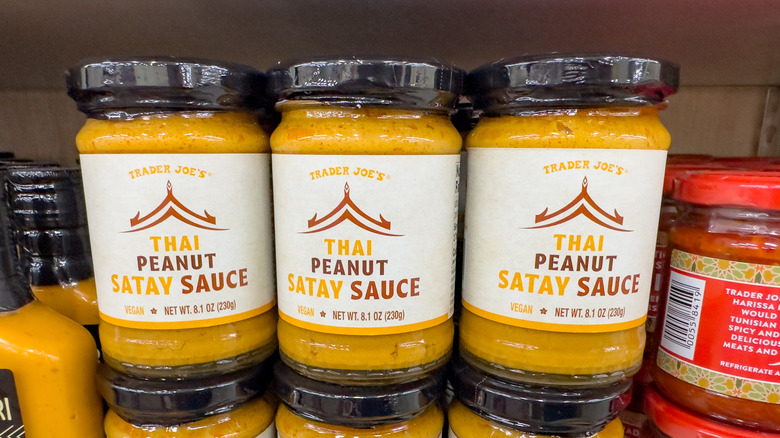 Jars of Trader Joe's Thai Peanut Satay Sauce in rows on store shelves