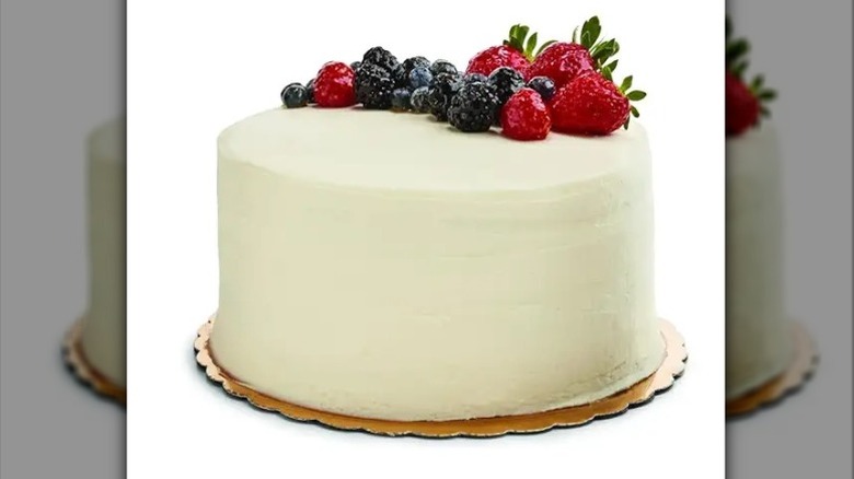 White frosted round cake with berries on a gold cake circle against a white background