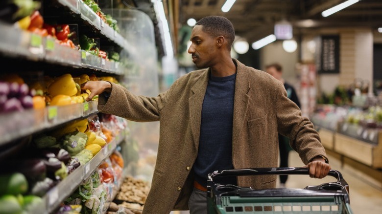 A man with a shopping cart picks out vegetables in the produce section of a grocery store