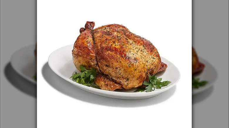 A rotisserie chicken on a white plate with garnish against a white background