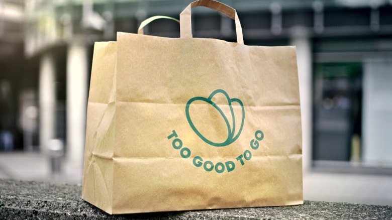 Too Good To Go paper bag sits on a concrete ledge with building in background