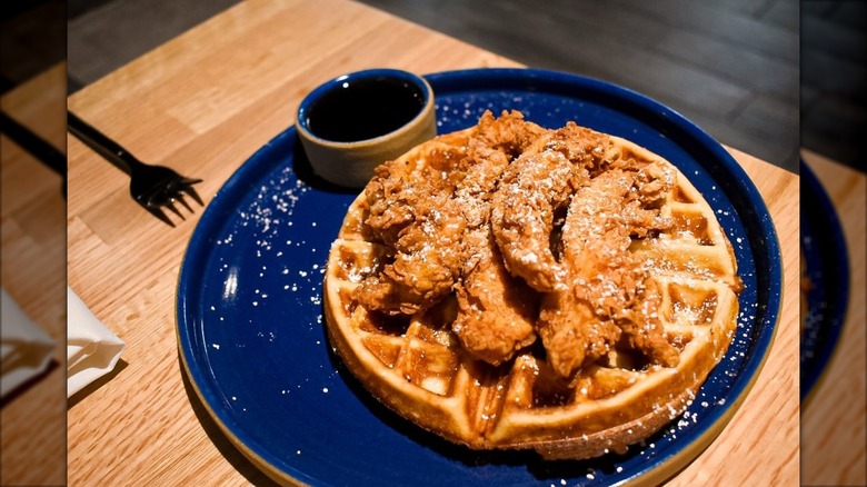 Chicken and waffles with powdered sugar on a blue plate