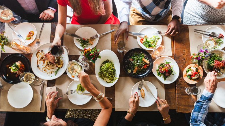 Group of people eating out at restaurant with lots of plates on the table