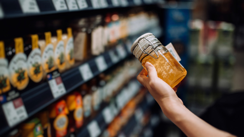 Hand holding glass jar of honey in store