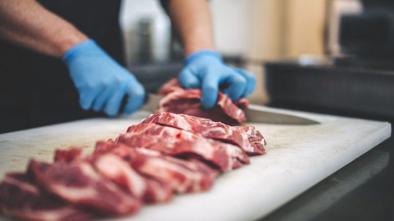 Gloved hands slicing raw meat
