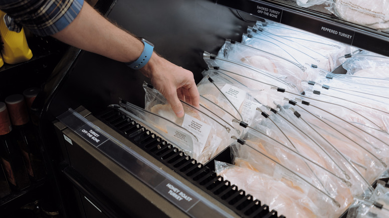 Hand taking deli meat from store cooler