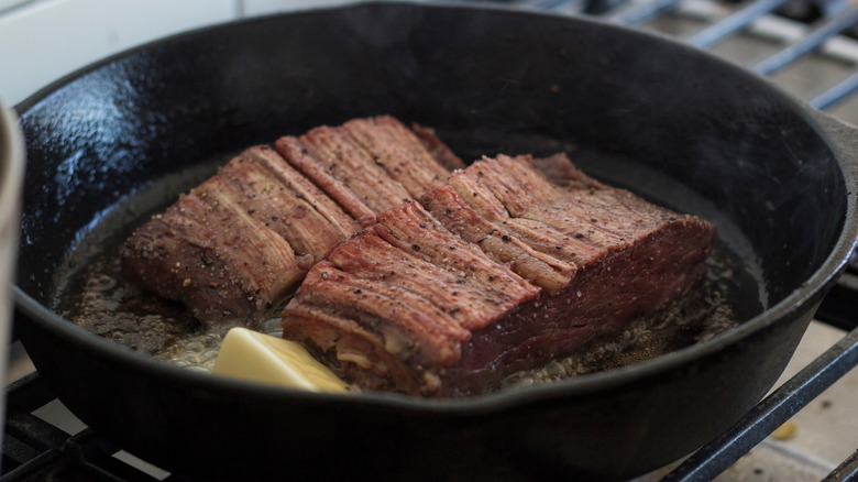 Ribeye caps cooking in black cast iron pan with butter