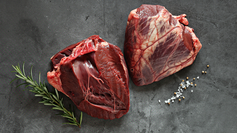 Raw untrimmed beef heart alongside sprig of rosemary