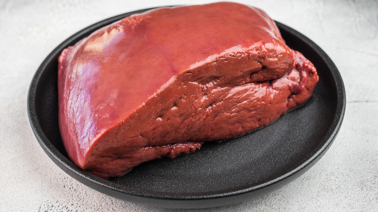 Whole raw beef liver on black plate