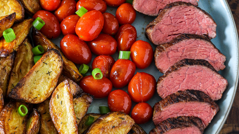 Seared and sliced teres major steak alongside roasted cherry tomatoes and potato wedges