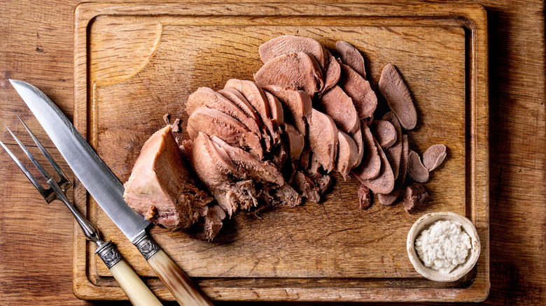 Cooked sliced beef tongue on wooden cutting board