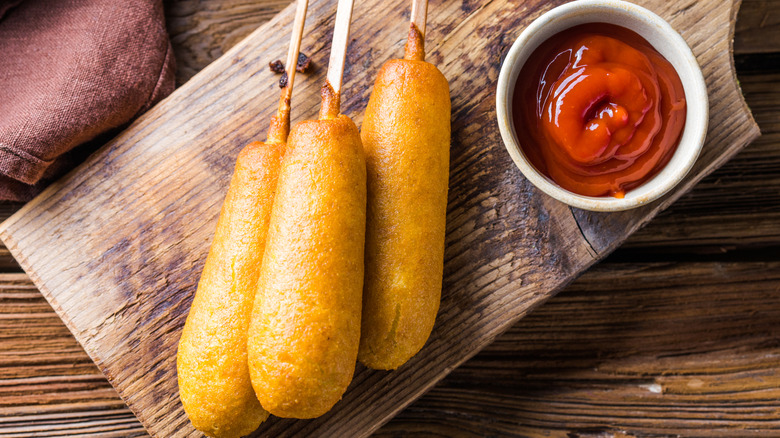 Corn dogs or sausage in roll with ketchup. Top view table scene over a wood background.