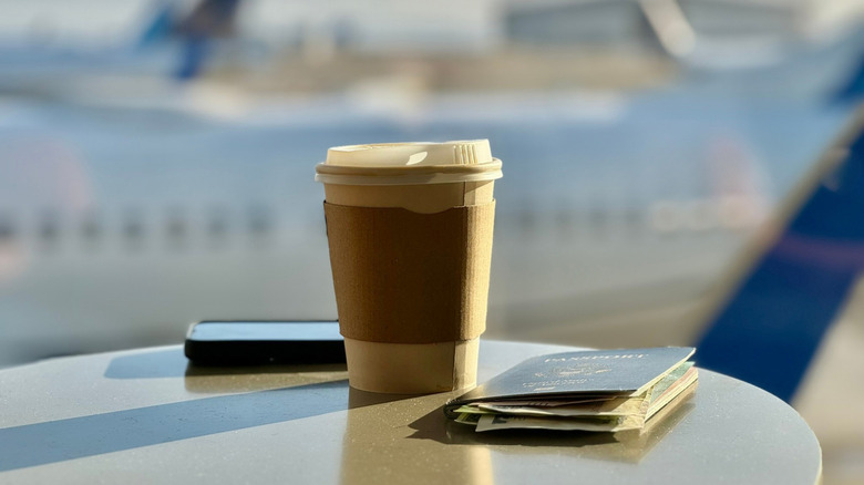 Cup of coffee on a table with a passport and a plane in the background