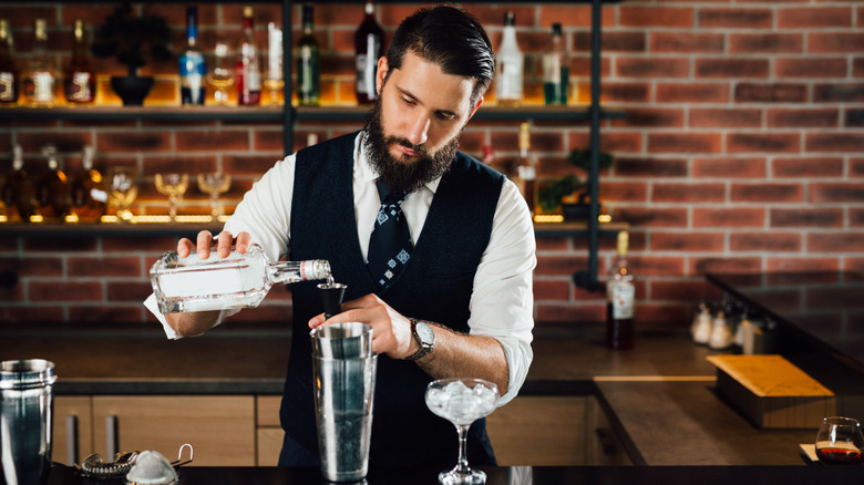 A barman measuring vodka over a cocktail shaker in upscale bar