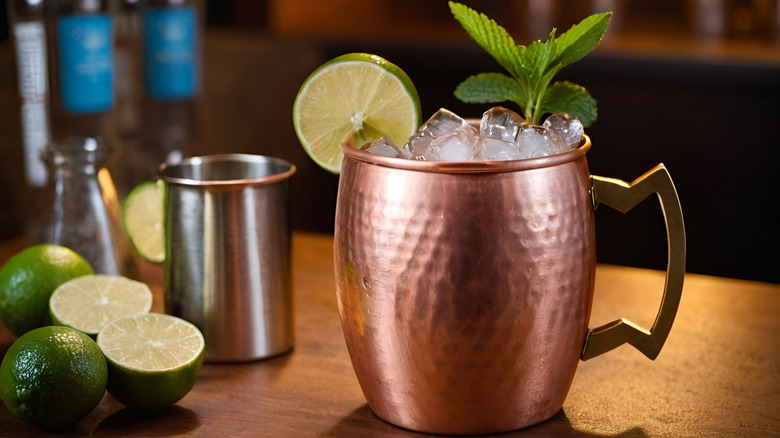 A Moscow mule in a copper cup, garnish with lime and mint on a bar, next to lime halves.
