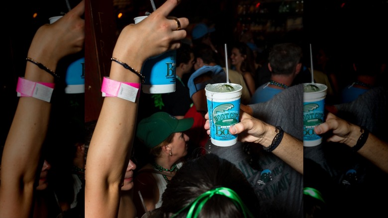 Close-up of people on a packed dance floor, holding cocktails in branded The Boot plastic cups