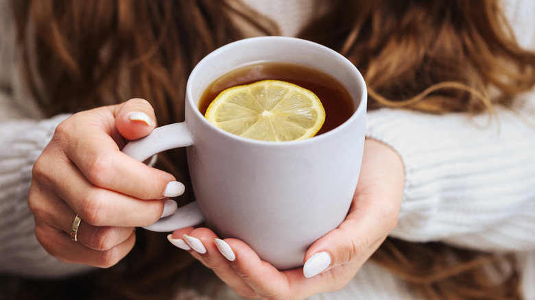 hand holding a mug of black tea with lemon slice
