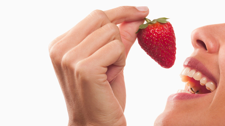A smiling woman eating a strawberry