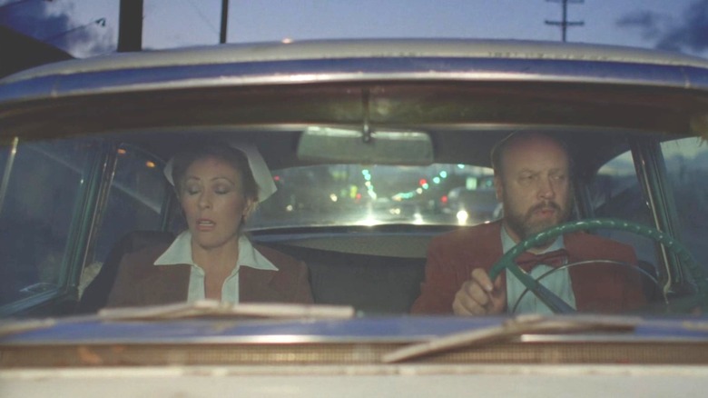 Mary Woronov sitting next to Paul Bartel in a car in "Eating Raoul"