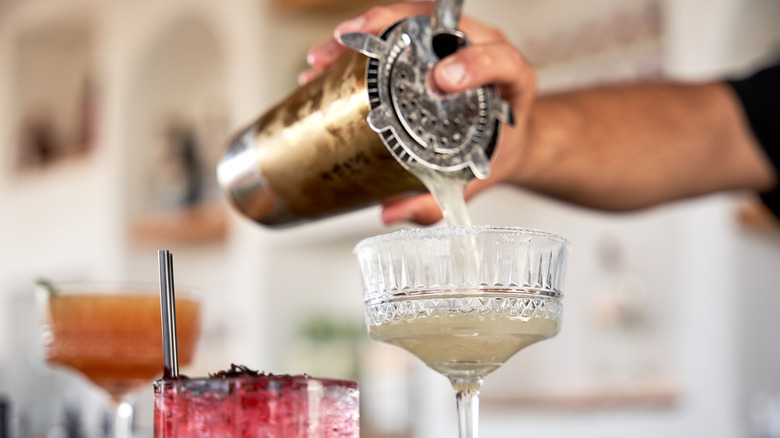 The bartender pours a margarita into the glass.