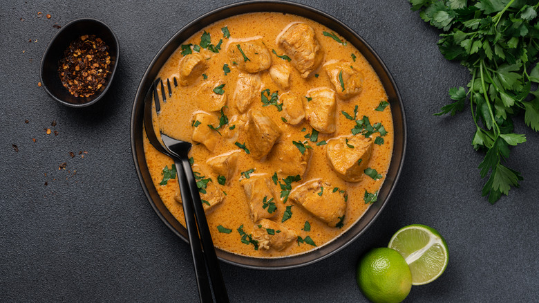 Indian butter chicken in a black bowl garnished with chopped parsley