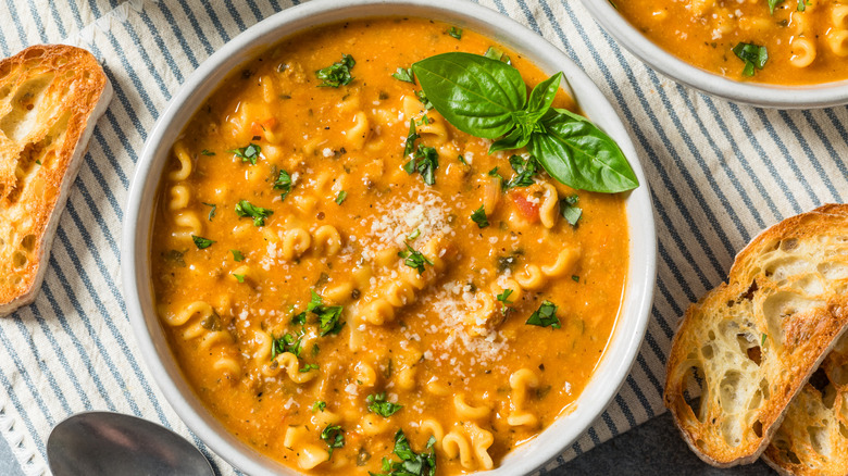 Top shot of a bowl of lasagna soup in a white bowl garnished with basil and surrounded by crisp bread slices
